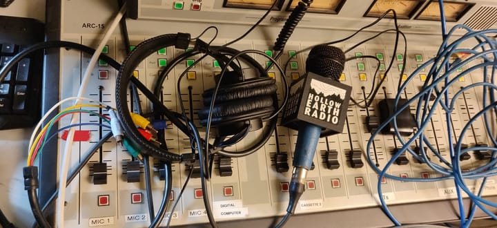 View from the KHUH booth: Audio cables of differing colors, a pair of over the ear headphones, and a handheld mic all resting on a radio mixing board.